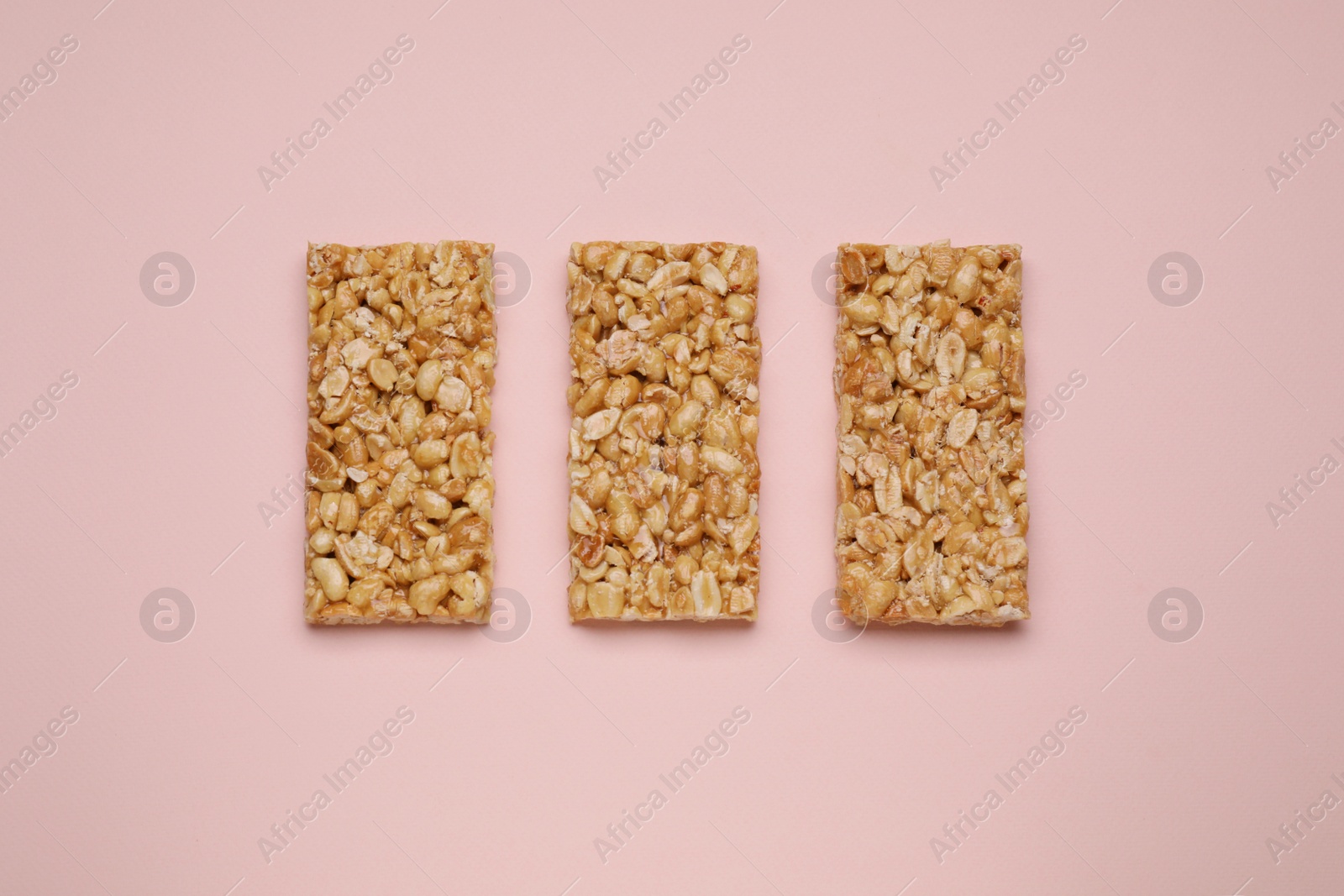 Photo of Tasty peanut bars (kozinaki) on pink background, flat lay