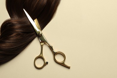 Photo of Professional scissors with brown hair strand on beige background, top view. Space for text