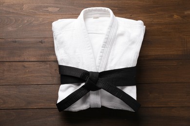 Photo of Martial arts uniform with black belt on wooden background, top view
