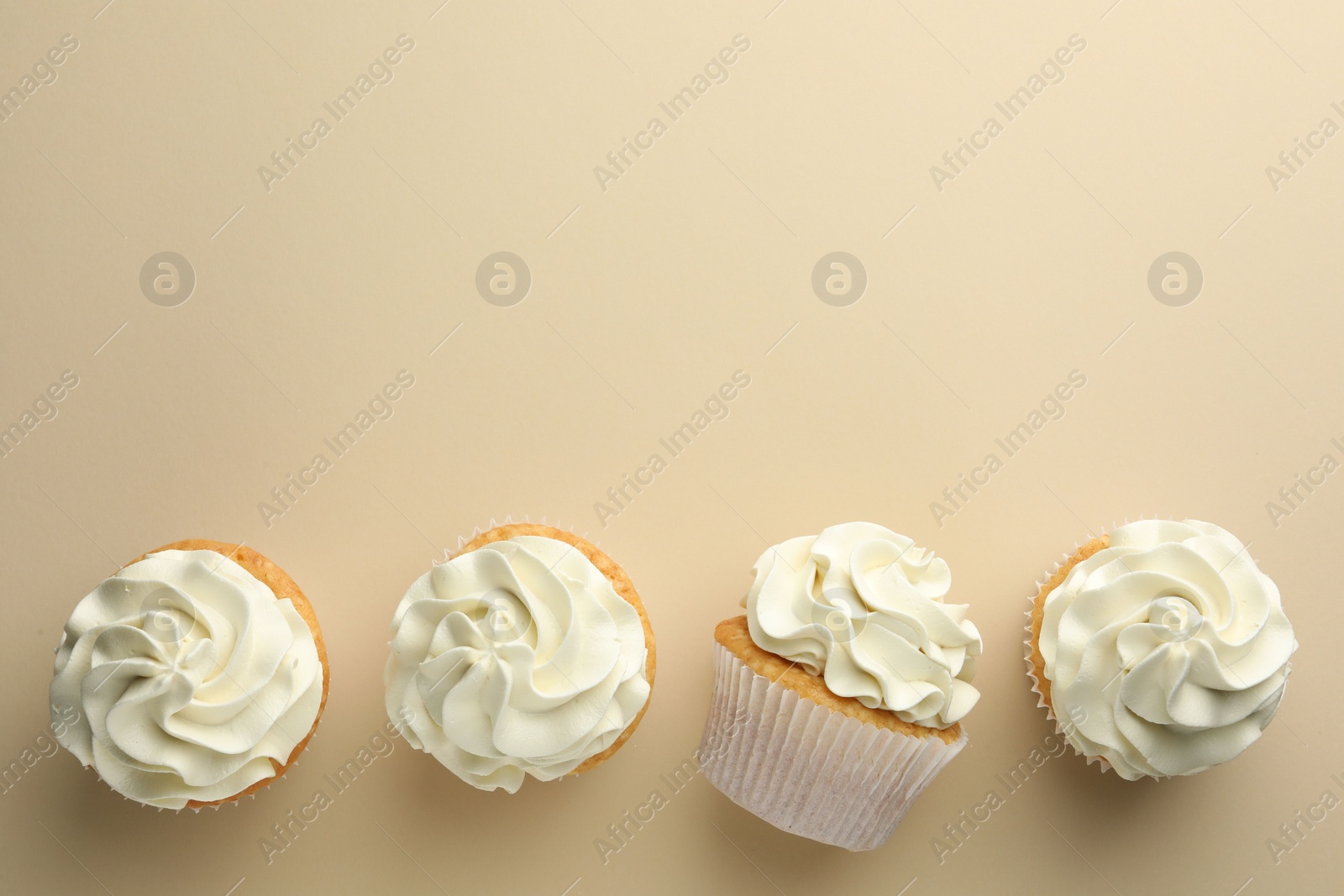 Photo of Tasty vanilla cupcakes with cream on beige background, top view. Space for text