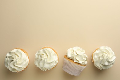 Photo of Tasty vanilla cupcakes with cream on beige background, top view. Space for text