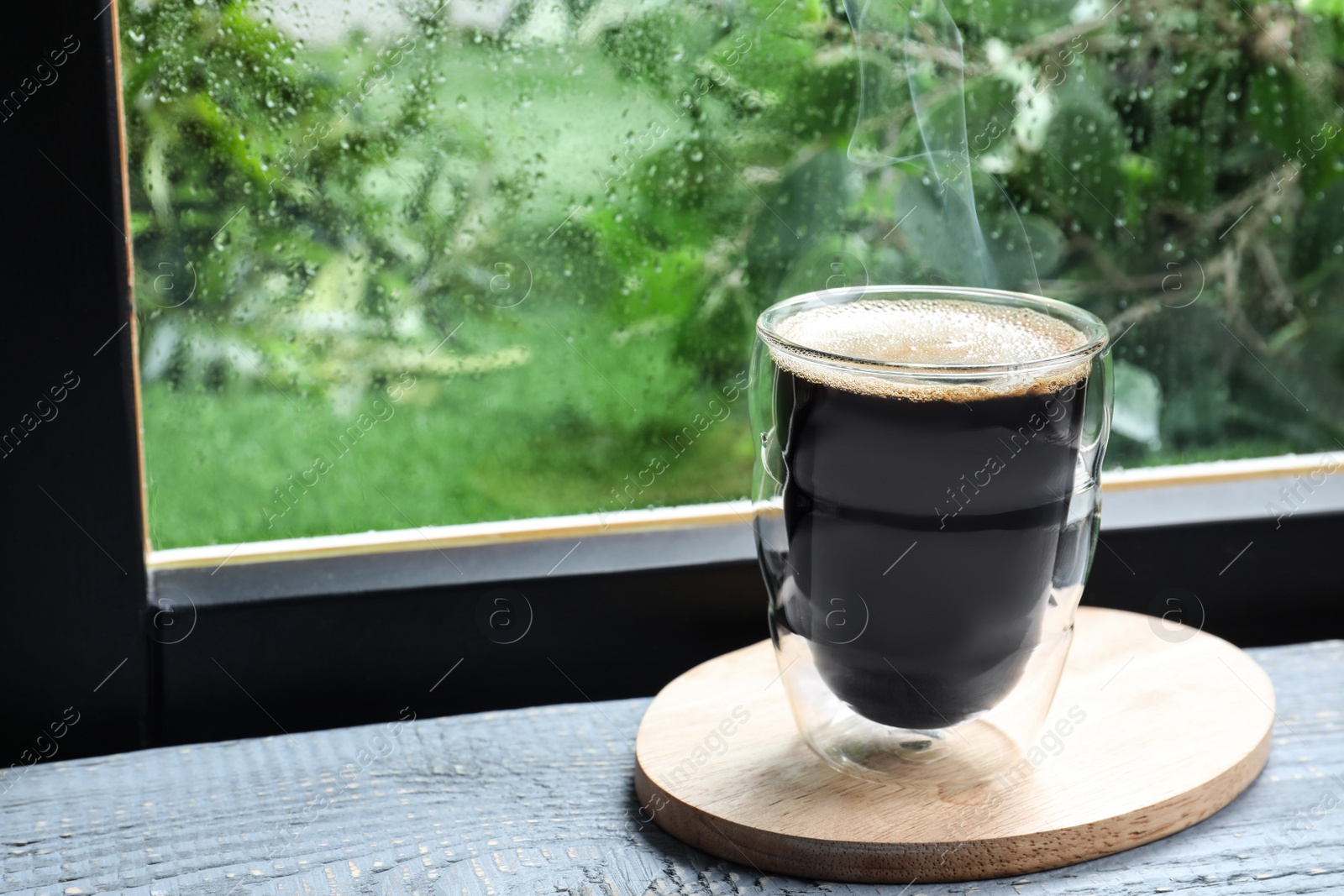 Photo of Glass of coffee on wooden windowsill, space for text. Rainy weather