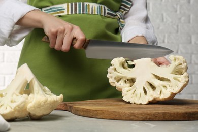Woman cutting fresh cauliflower at light grey table, closeup
