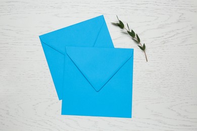 Photo of Turquoise envelopes and green twig on white wooden table, flat lay
