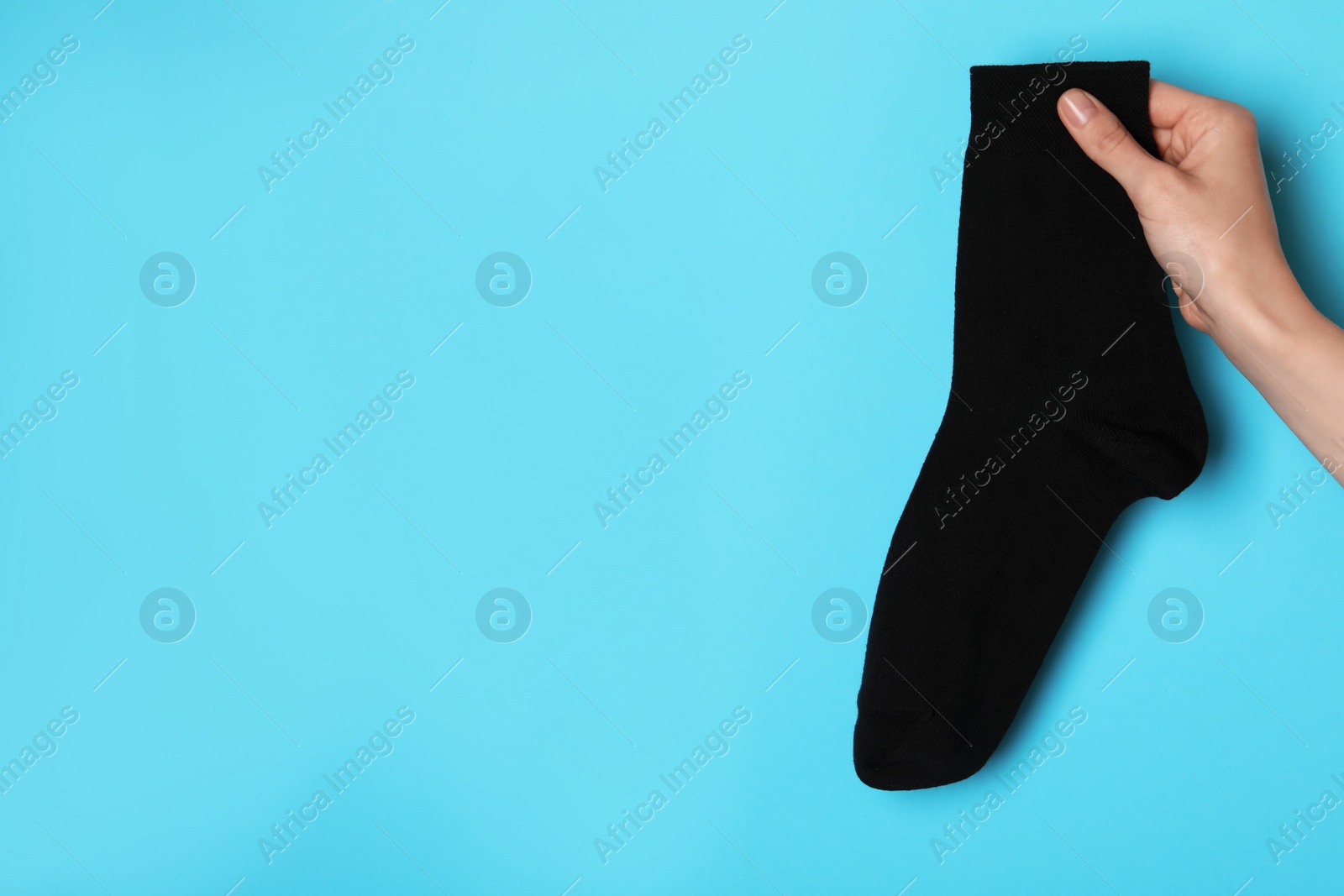 Photo of Woman holding black sock on light blue background, closeup. Space for text