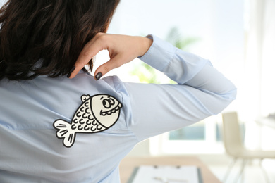 Photo of Woman with paper fish on back indoors, closeup. April fool's day