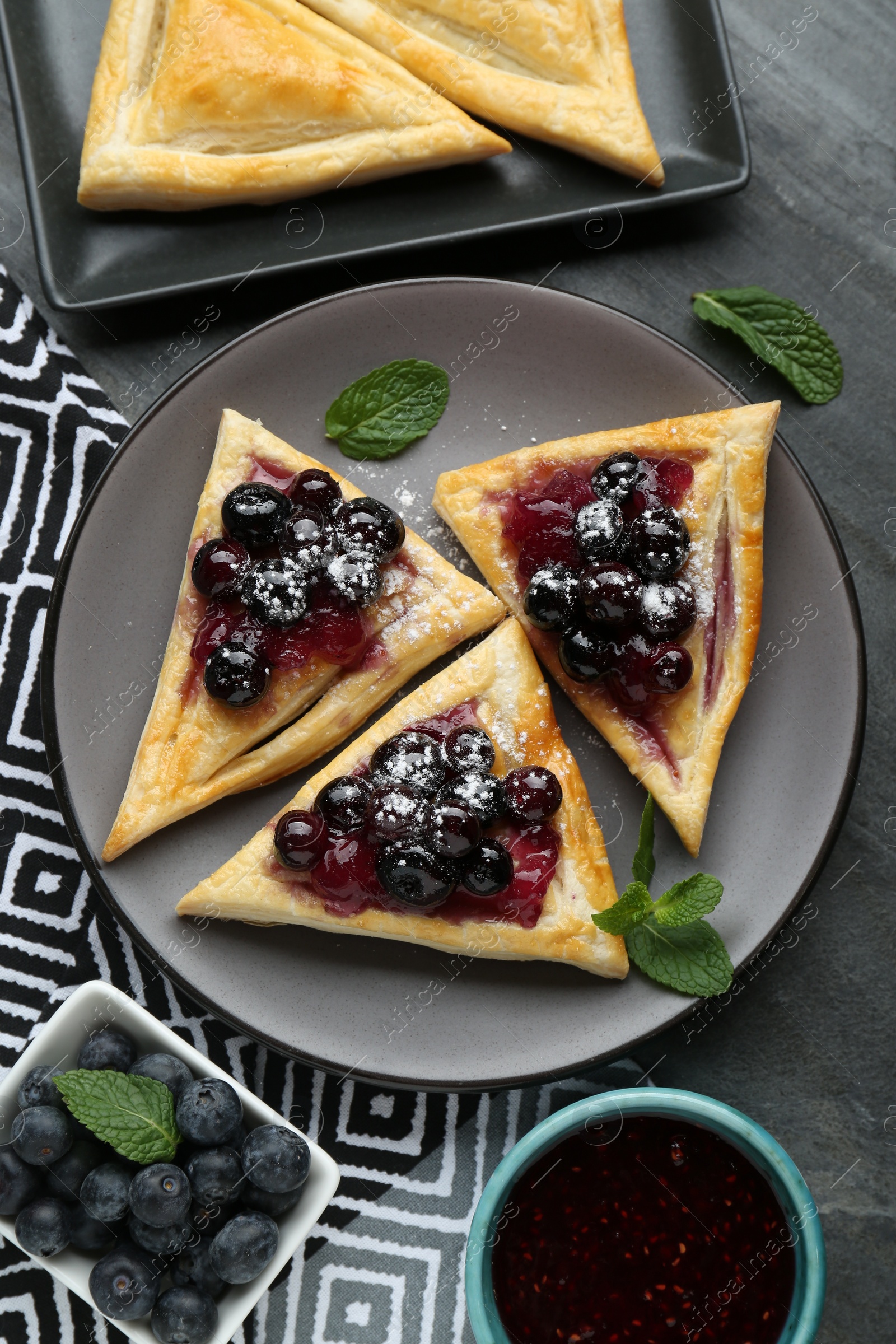 Photo of Fresh tasty puff pastry with sugar powder, jam, sweet berries and mint served on grey table, flat lay