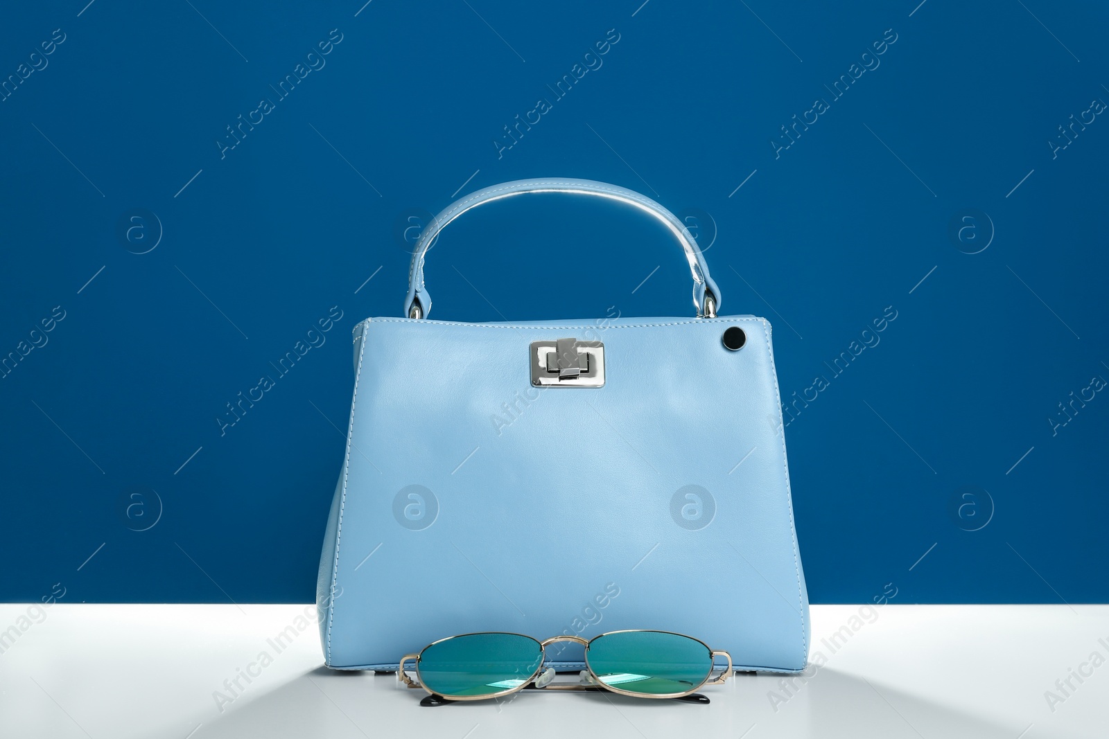 Photo of Stylish woman's bag and sunglasses on white table