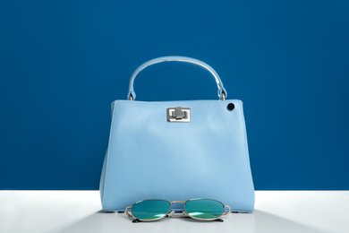 Photo of Stylish woman's bag and sunglasses on white table