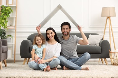 Housing concept. Happy husband holding plastic roof over his family while sitting on floor at home