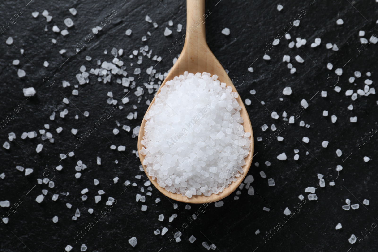 Photo of Organic white salt and spoon on black table, top view