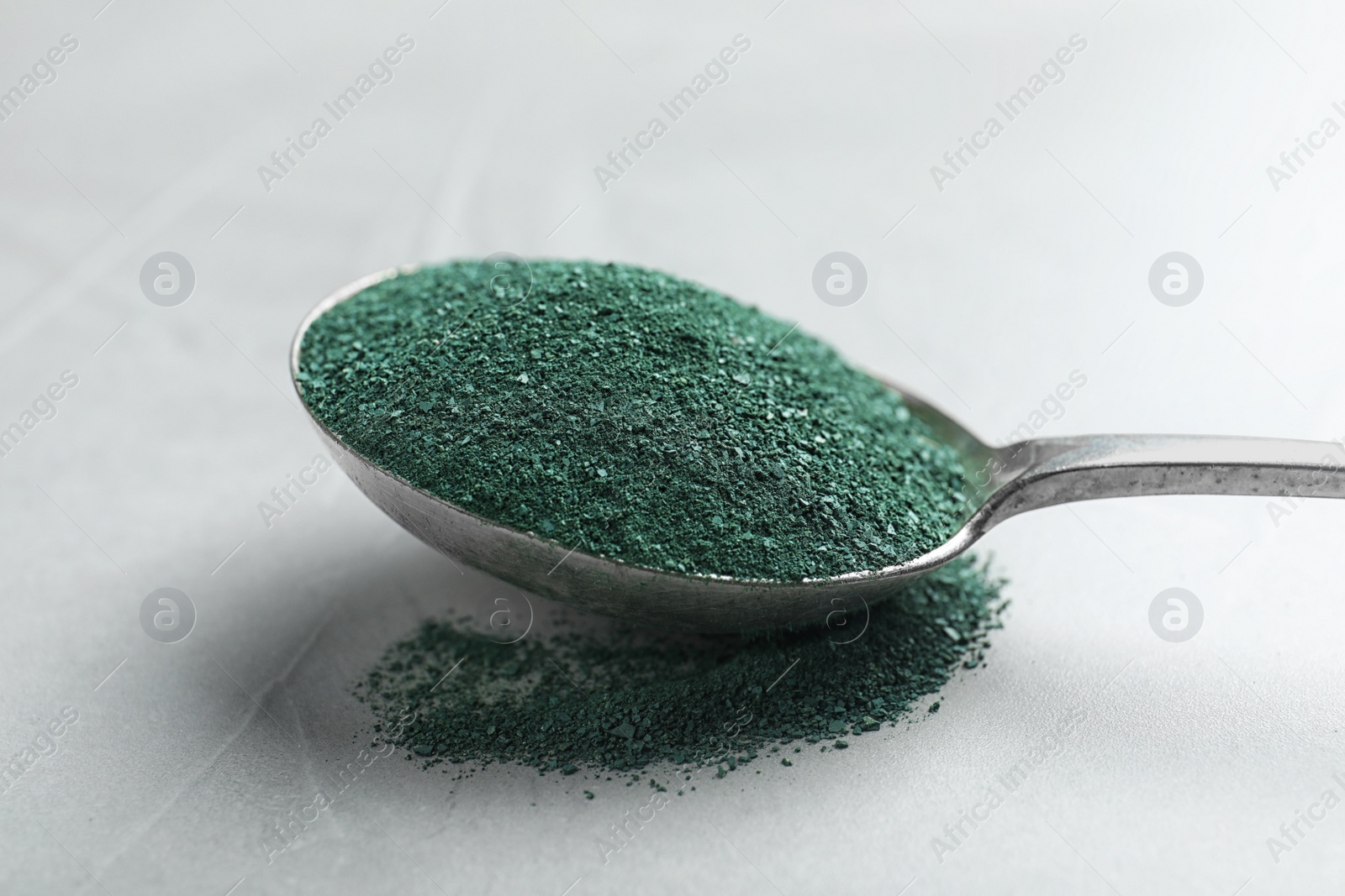 Photo of Spoon of spirulina algae powder on grey background, closeup