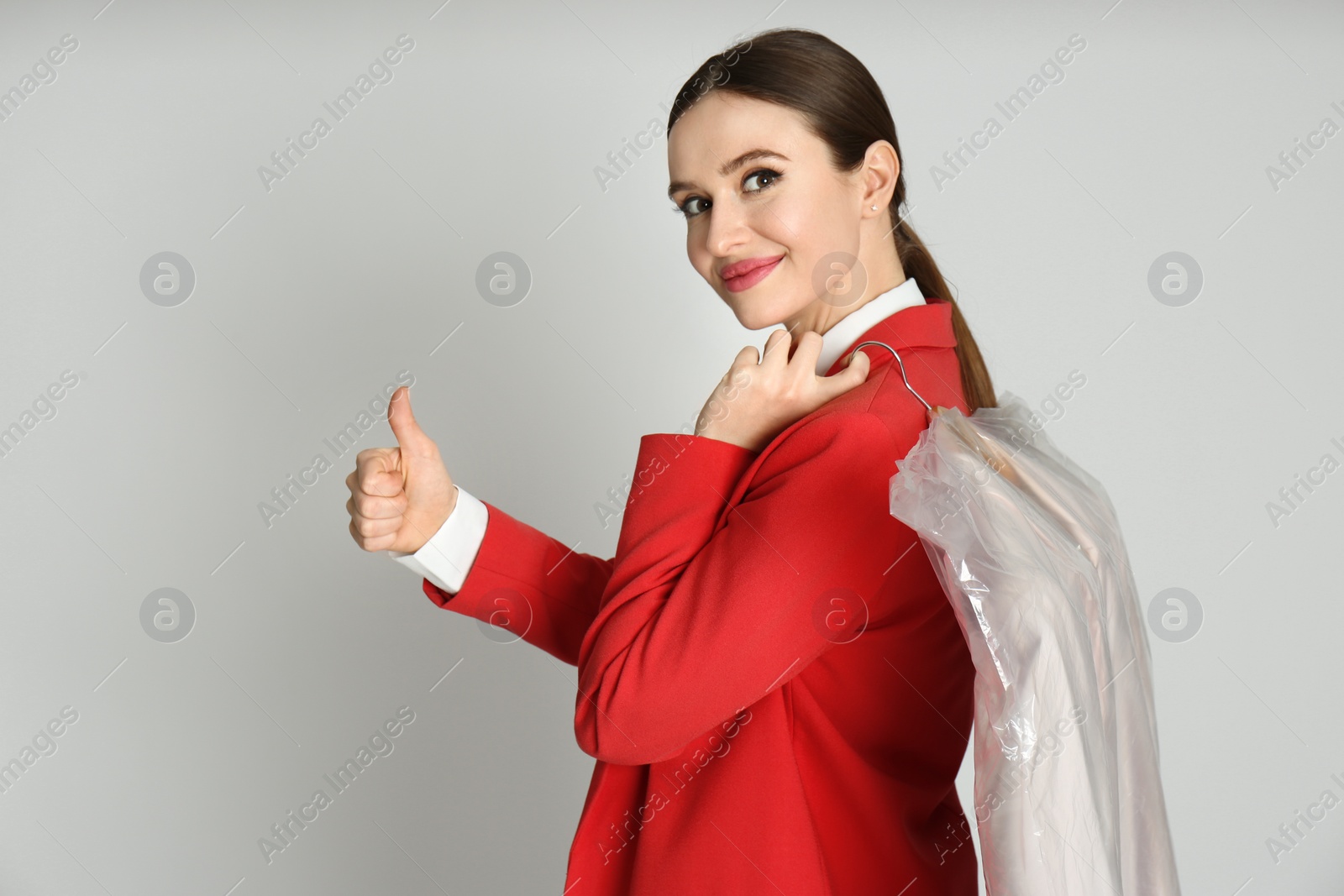 Photo of Young woman holding hanger with jacket on light grey background. Dry-cleaning service