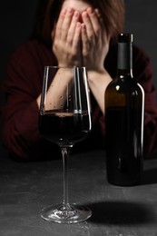 Photo of Alcohol addiction. Woman covering her face at dark textured table, focus on glass of red wine