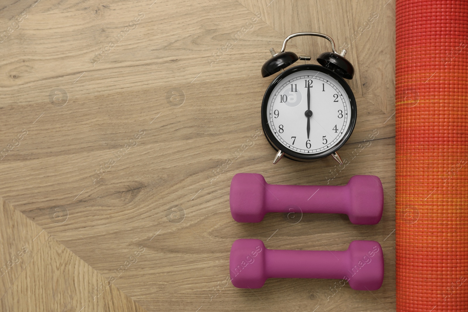 Photo of Alarm clock, yoga mat and dumbbells on wooden background, flat lay with space for text. Morning exercise