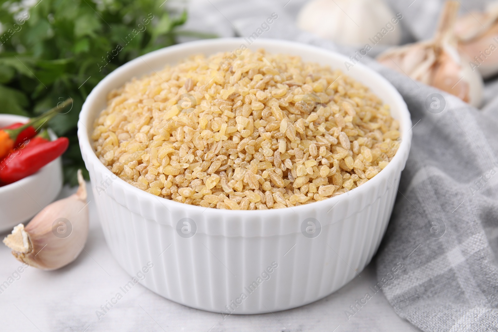 Photo of Raw bulgur in bowl and spices on table, closeup