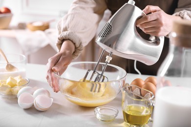 Woman making dough with mixer in bowl at table, closeup