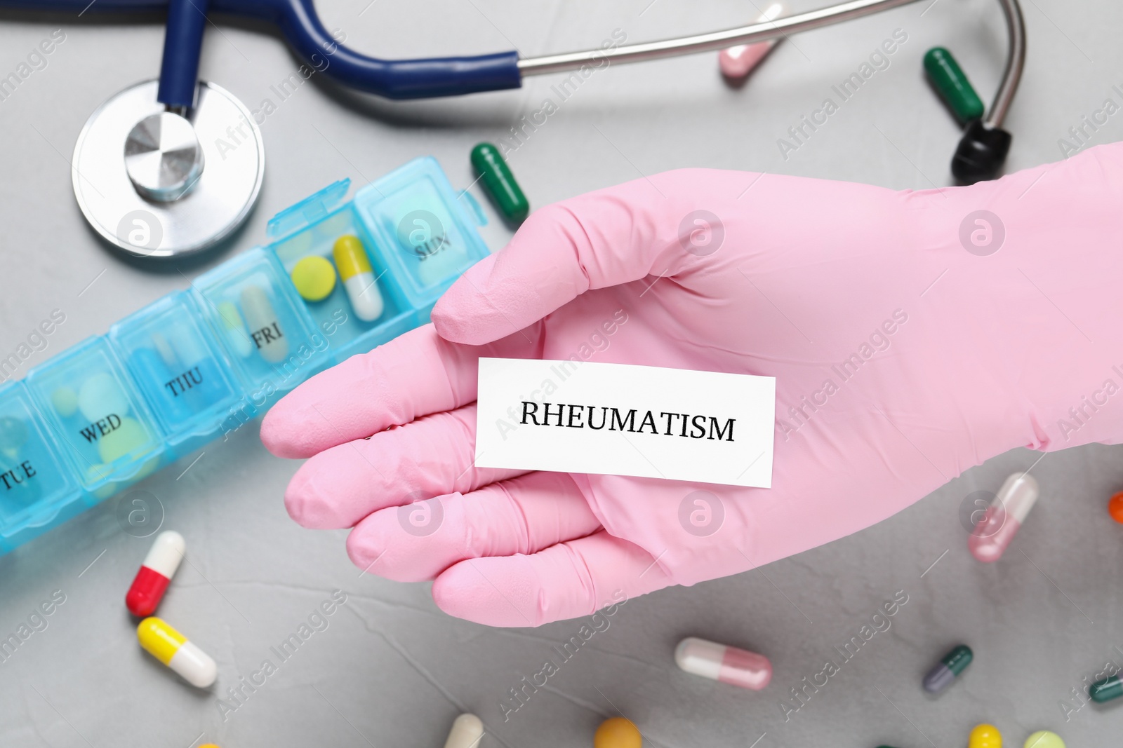 Photo of Doctor in glove holding sheet of paper with word Rheumatism above grey table, closeup