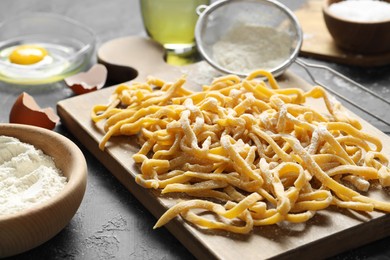 Photo of Board with homemade pasta and ingredients on dark textured table, closeup