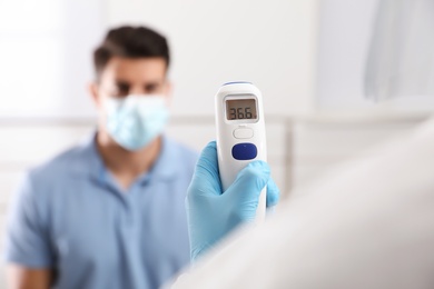 Photo of Doctor measuring man's temperature indoors, closeup. Prevent spreading of Covid-19