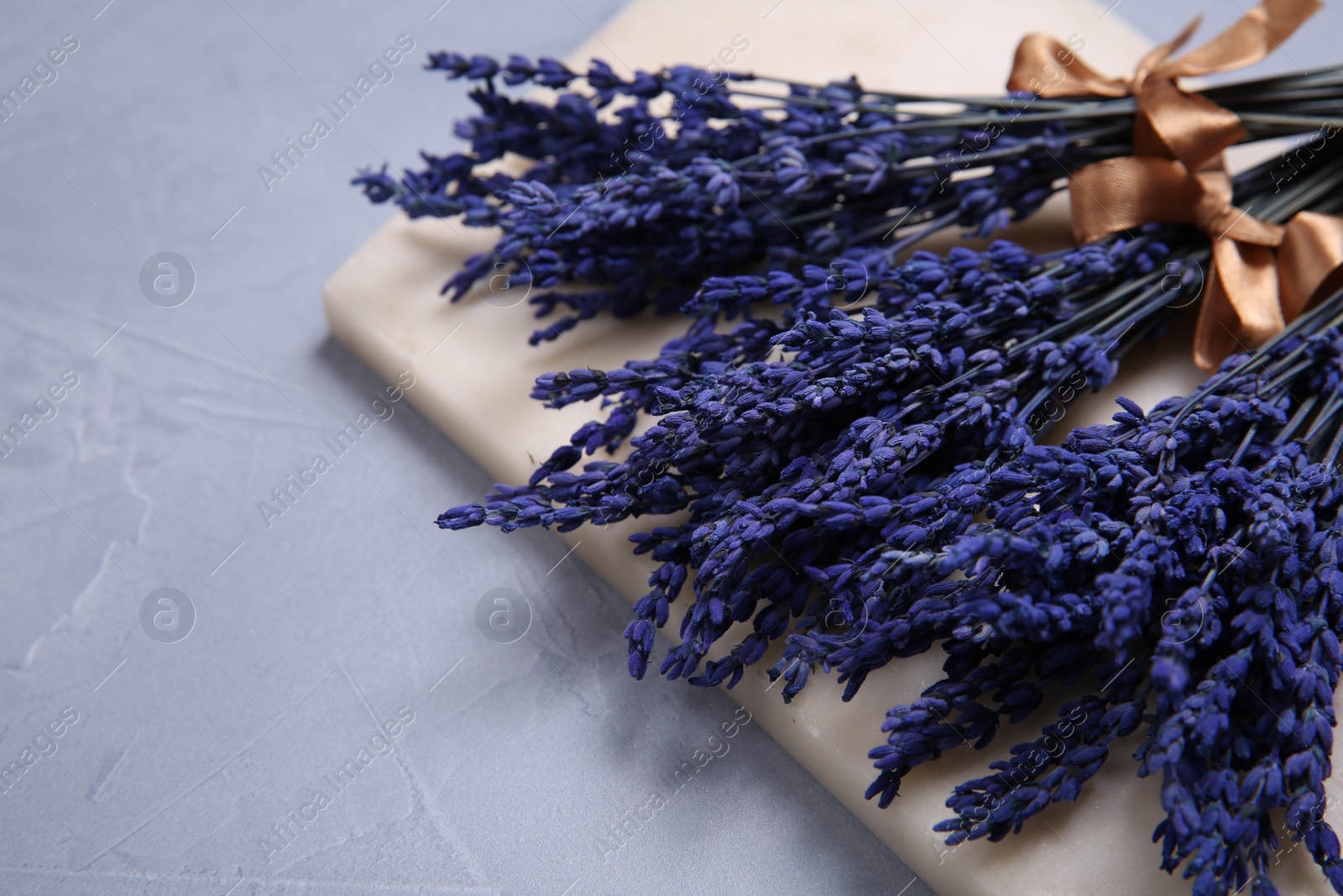 Photo of Bouquets of beautiful preserved lavender flowers and stone board on light grey textured table, space for text