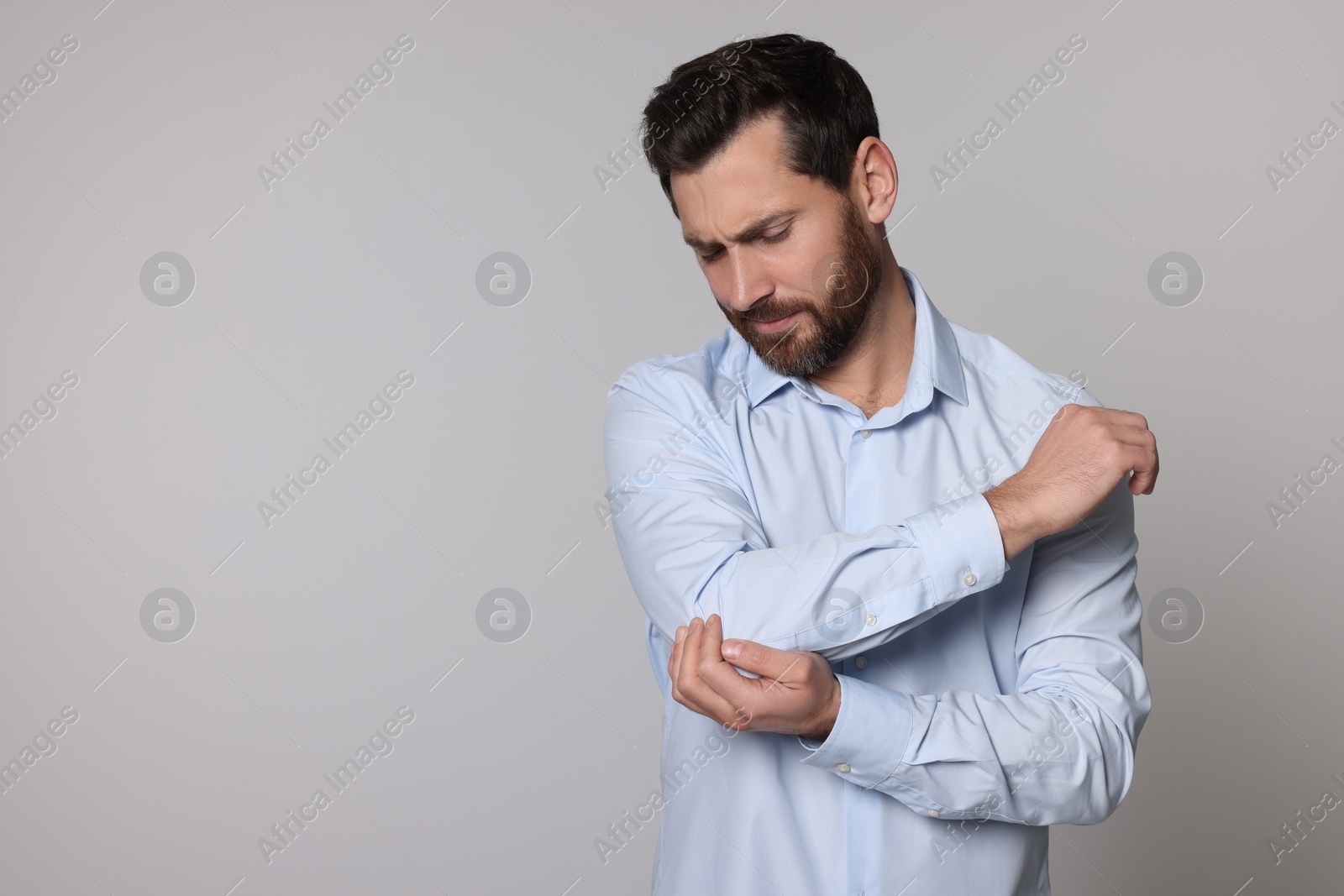 Photo of Man suffering from pain in his elbow on light background, space for text. Arthritis symptoms