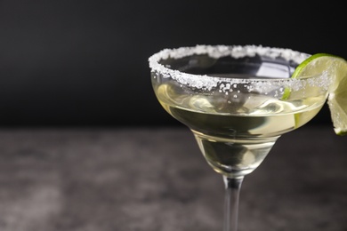 Glass of lemon drop martini cocktail with lime slice on table against black background, closeup. Space for text