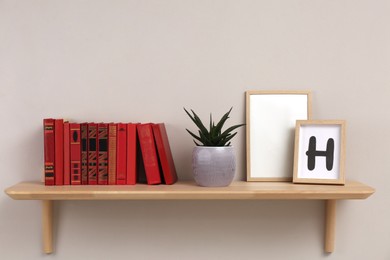 Photo of Wooden shelf with different books, houseplant and frames on light wall