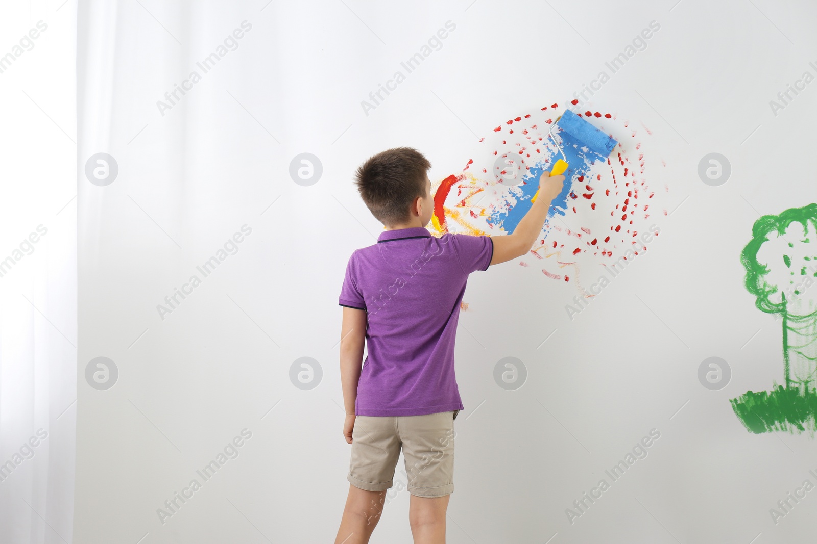 Photo of Little child painting wall with roller brush indoors