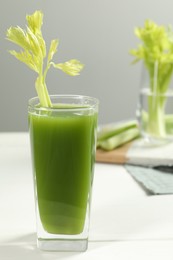 Glass of fresh celery juice on white table