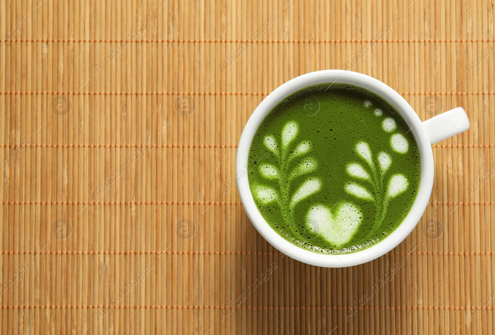 Photo of Delicious matcha latte in cup on bamboo mat, top view. Space for text