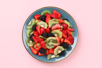 Plate of yummy fruit salad on pink background, top view