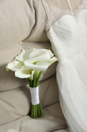 Photo of Beautiful calla lily flowers tied with ribbon and wedding dress on sofa