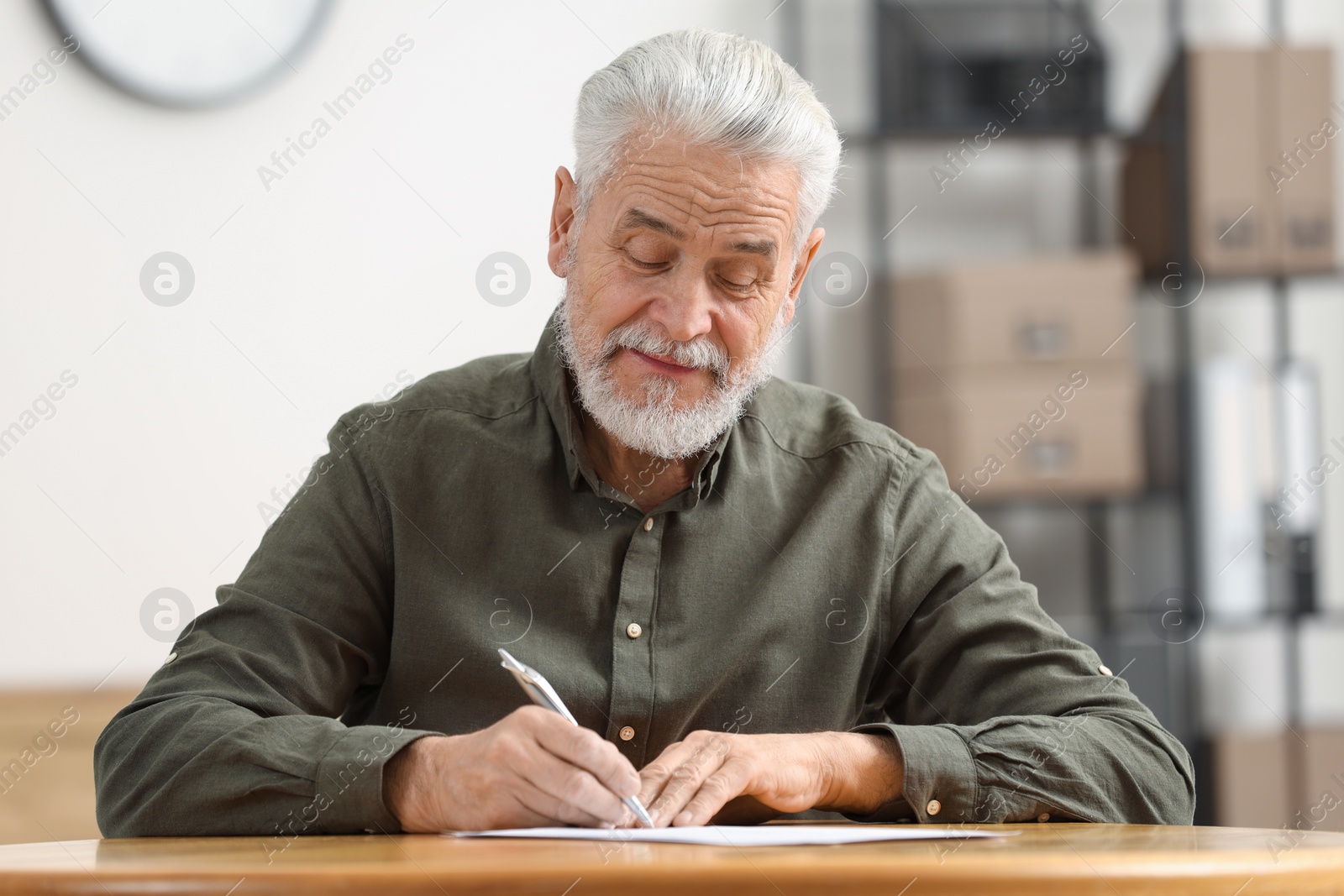 Photo of Senior man signing Last Will and Testament at table indoors