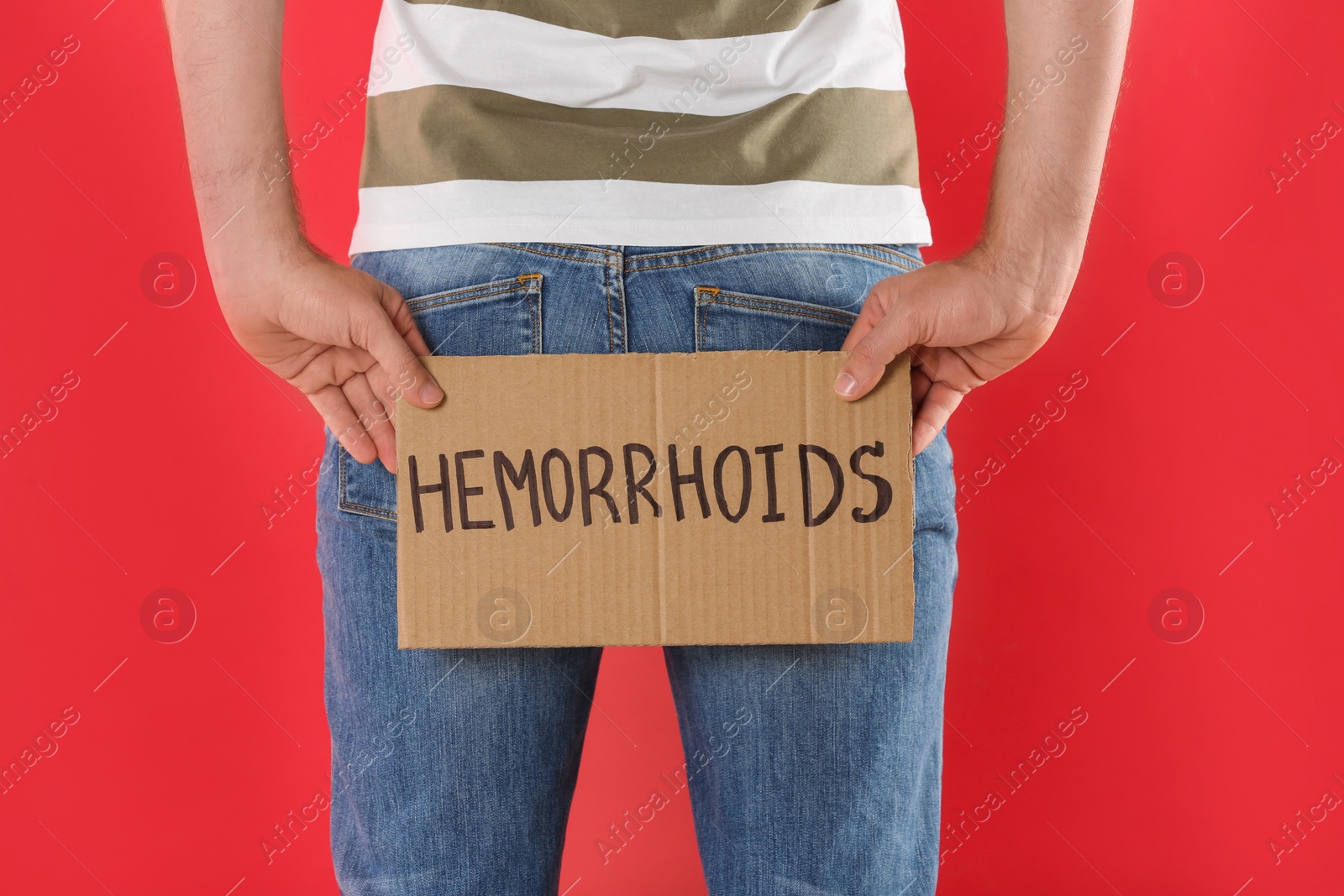 Photo of Man holding carton sign with word HEMORRHOIDS on red background, closeup