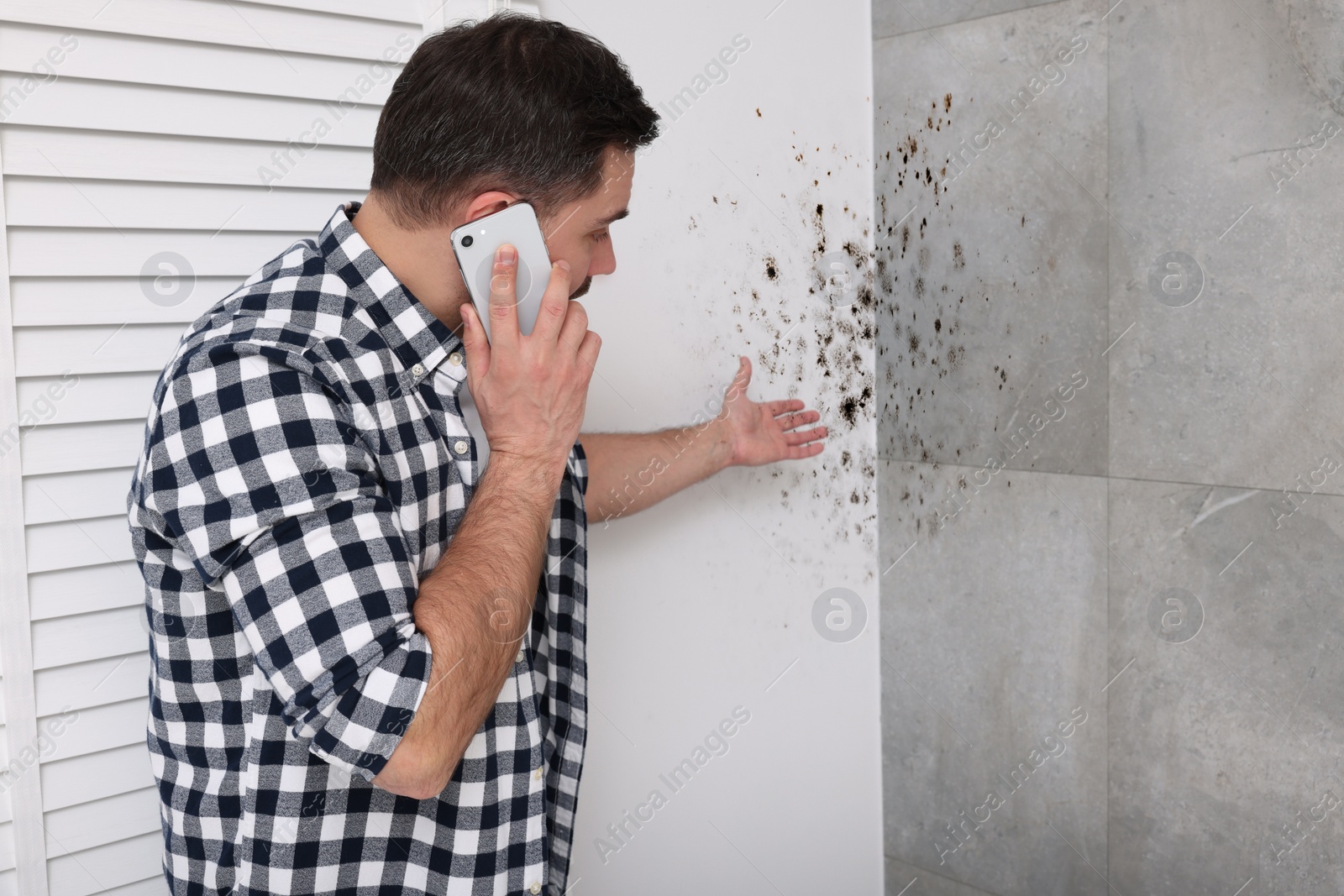 Image of Mold removal service. Man talking on phone and looking at affected walls in room