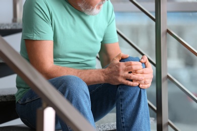 Photo of Senior man suffering from knee pain indoors, closeup