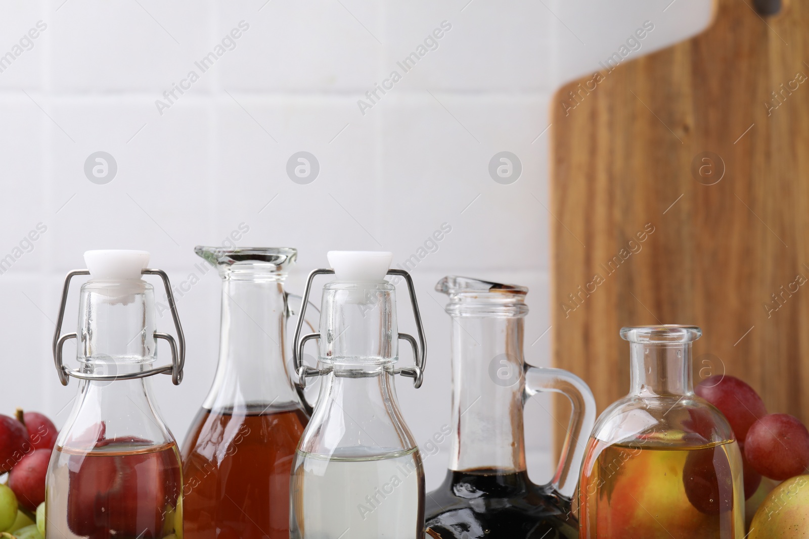 Photo of Different types of vinegar and fresh fruits against blurred background