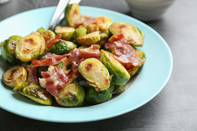 Photo of Delicious roasted Brussels sprouts with bacon served on black table, closeup