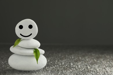 Photo of Stack of stones with drawn happy face and leaves on grey background, space for text. Zen concept