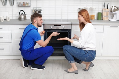 Housewife with repairman near modern oven in kitchen