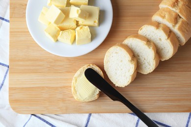 Photo of Cut baguette with fresh butter on checkered tablecloth, top view