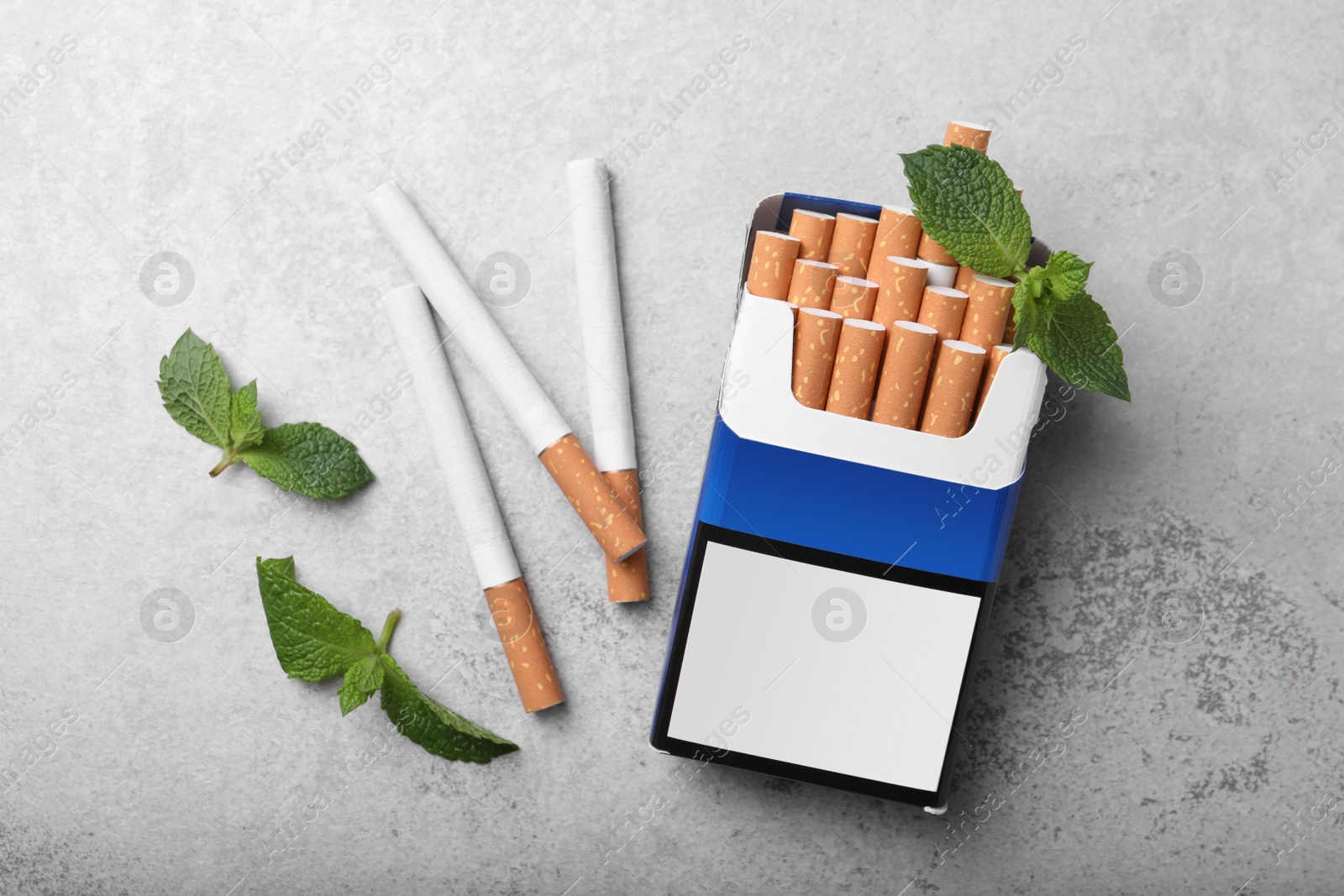 Photo of Pack of menthol cigarettes and mint leaves on grey table, flat lay