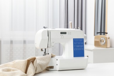 Photo of Sewing machine and fabric on white table in workshop