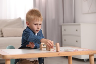 Photo of Cute little boy playing with wooden toys at table indoors, space for text