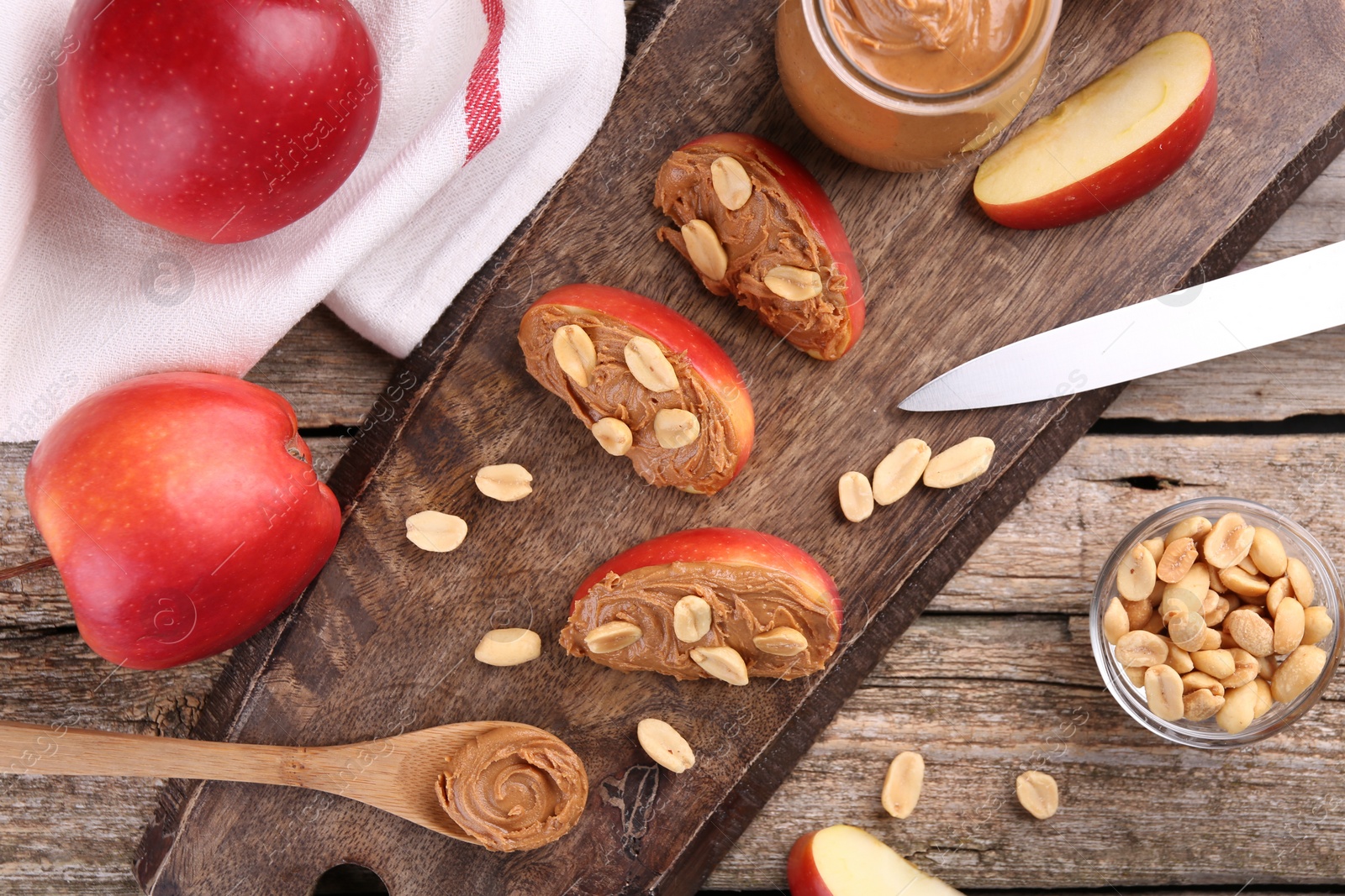 Photo of Fresh apples with peanut butter, knife and spoon on wooden table, flat lay