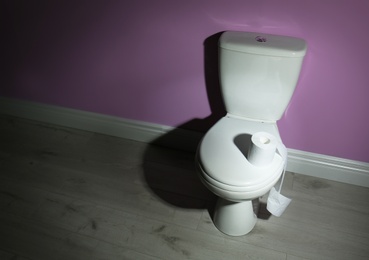 Photo of New ceramic toilet bowl and roll of toilet paper near color wall