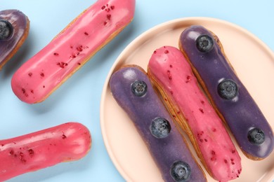 Photo of Delicious eclairs covered with glaze on light blue background, top view