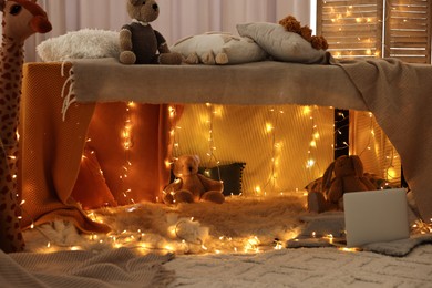 Photo of Beautiful play tent decorated with festive lights and toys at home