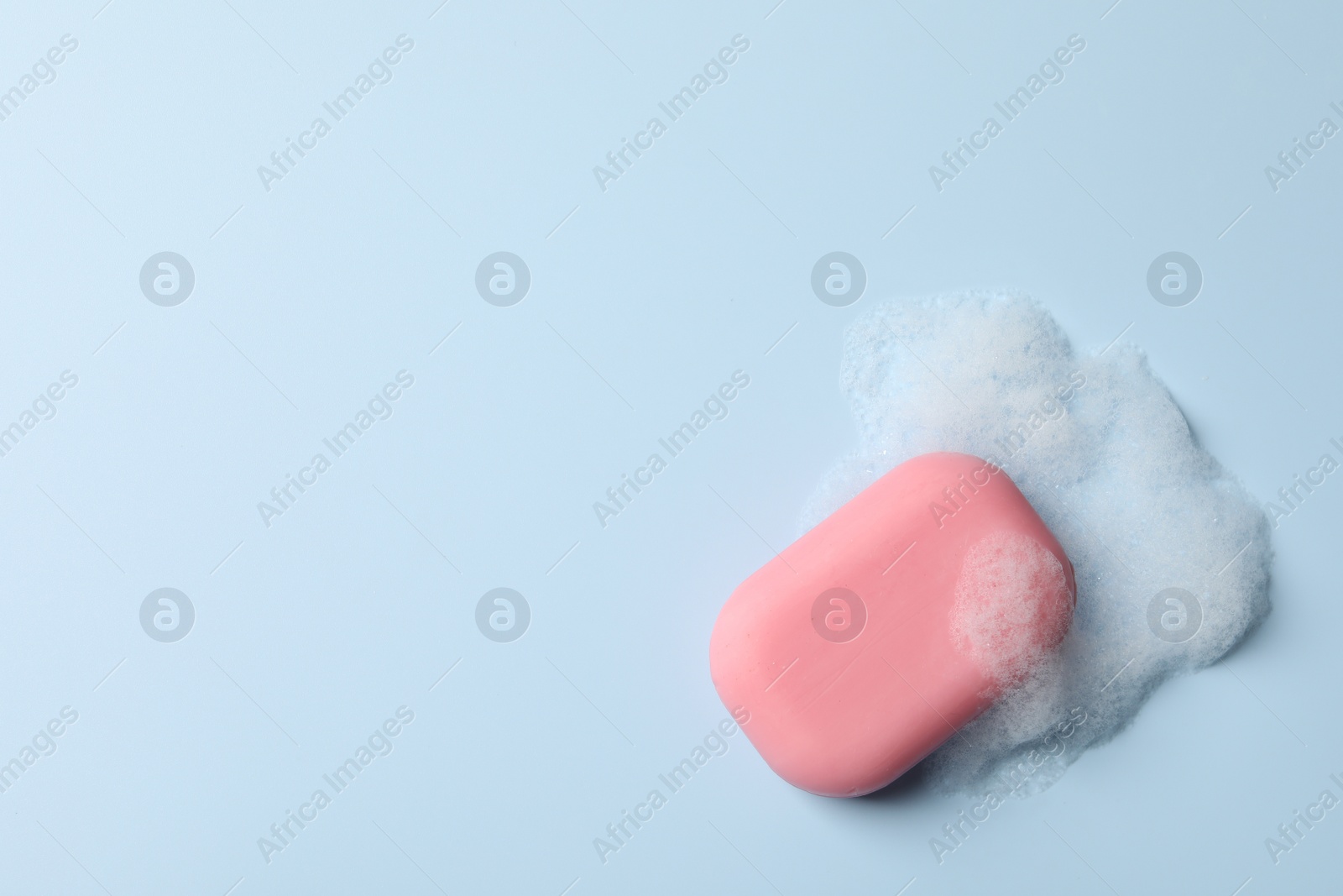 Photo of Soap with fluffy foam on light blue background, top view. Space for text